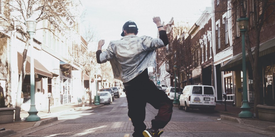 Youth jumping in celebration, standing in street, back to camera.