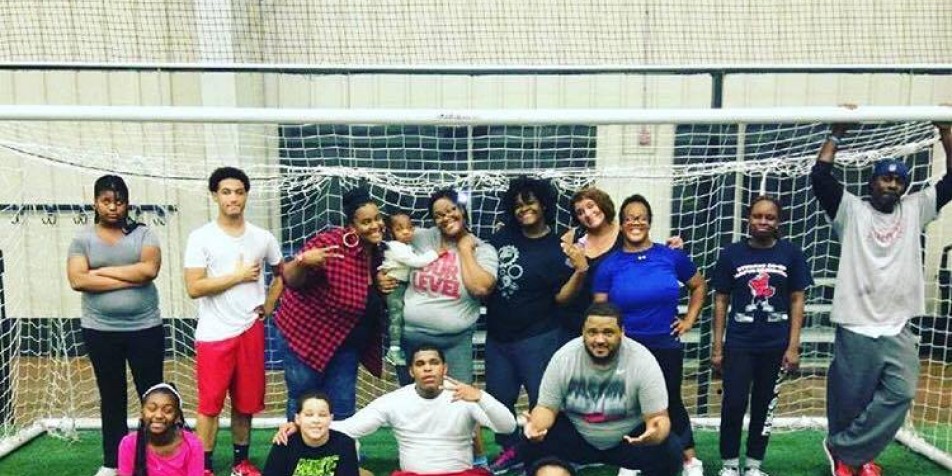 Group photo of adults and children standing around soccer goal.