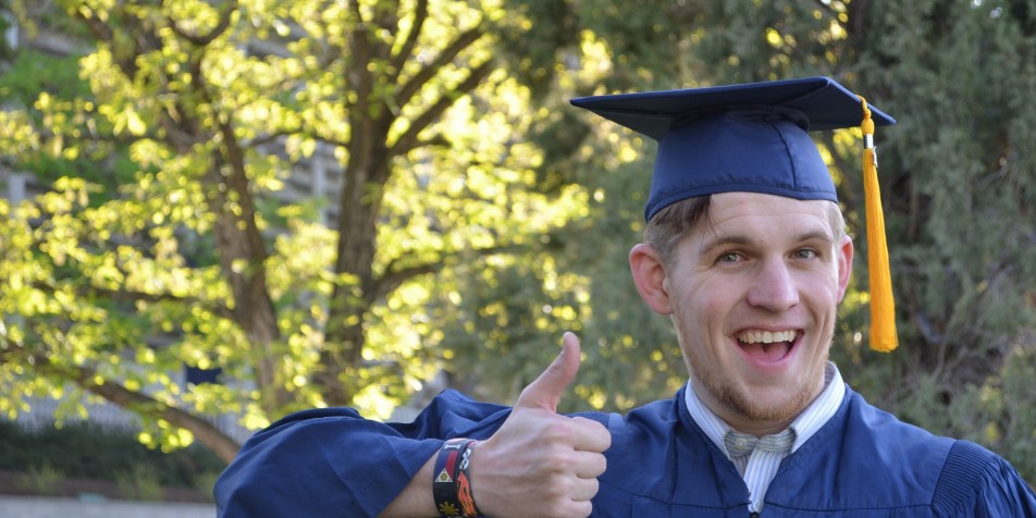 Young man in graduation cap, giving thumbs up.