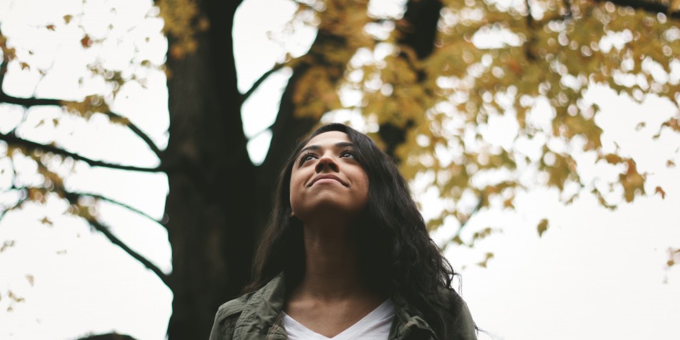 Girl looking up, in front of tress.