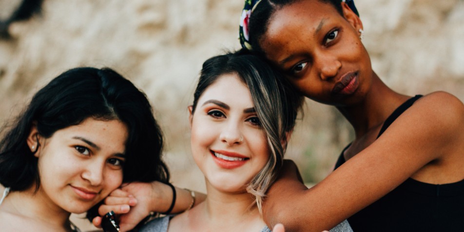 Photo of three girls leaning against each other, facing camera.