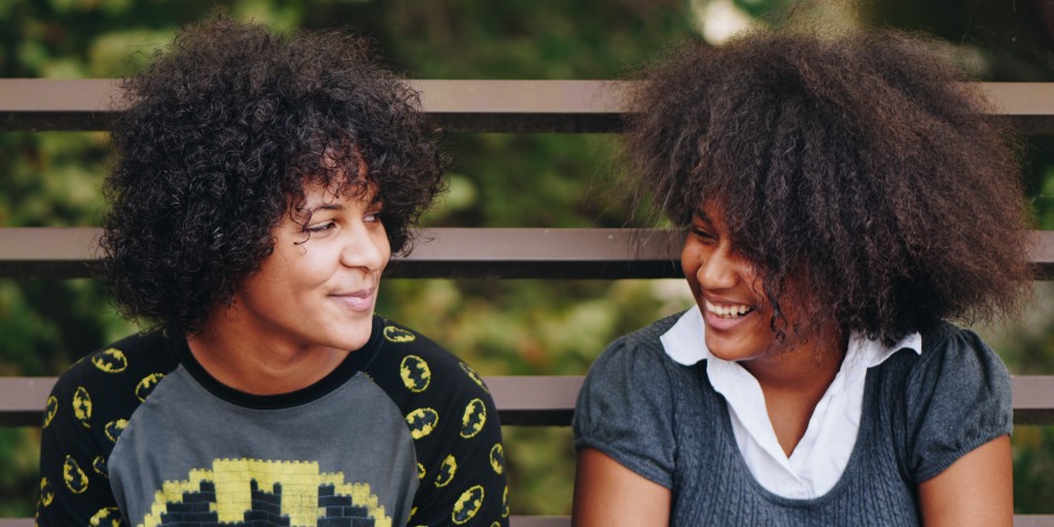 Photo of two youth sitting on a bench, facing each other laughing.