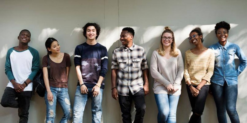 7 youth standing against a wall, smiling at the camera.