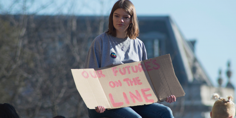Young woman holding protest sign reading "Our future's on the line."