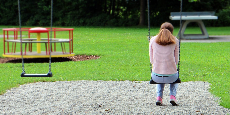 Back of teen sitting on swing, looking forlorn 