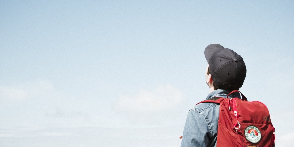 An image of a young man wearing a cap and red backpack looking at the sky.
