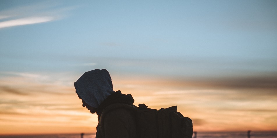 image of a young man, walking while wearing a hood and large backpack. 