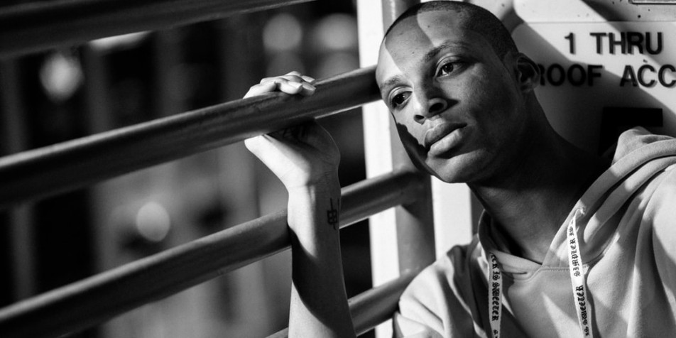 A young man leaning against window bars and staring into the distance. 