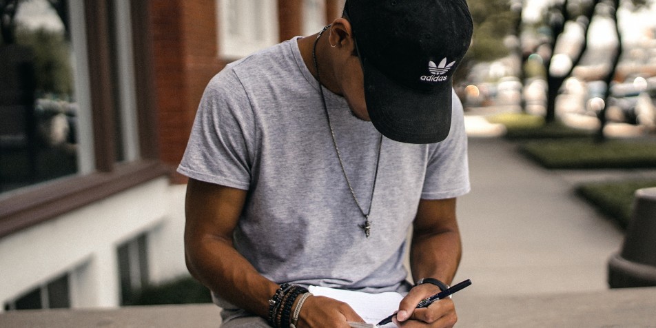 young man with baseball cap writes in a notebook 