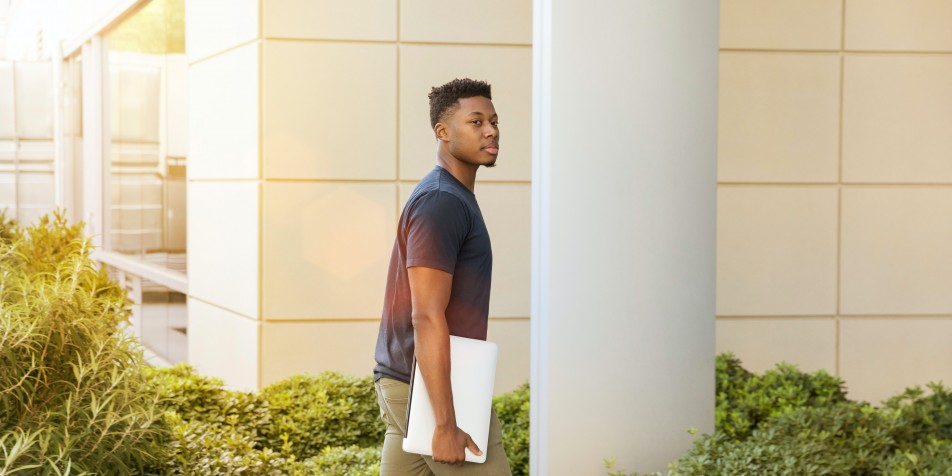 a young man walking on campus with books in hand. 