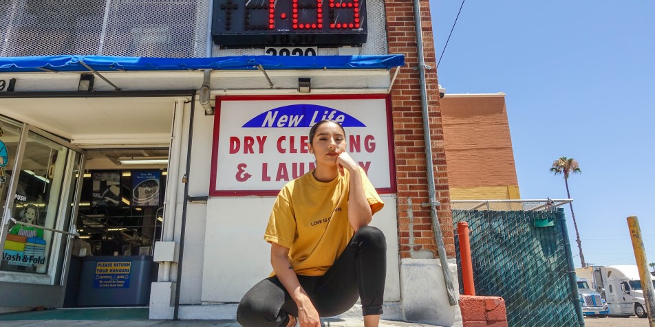 Photo of a youth sitting/kneeling in front of a corner laundromat
