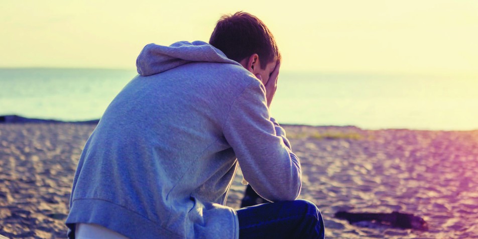 youth with head in hands on beach