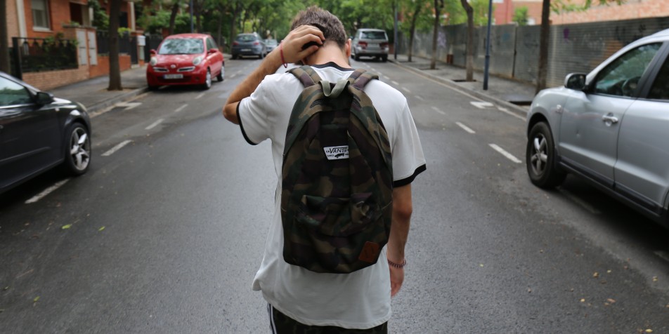 a young man with a camo backpack walking down a street