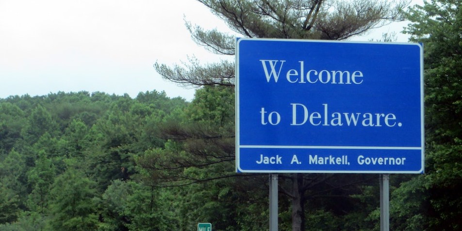 Blue "Welcome to Delaware" sign in front of trees