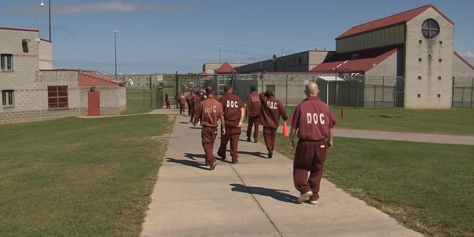 adults in red jumpsuits walking towards prison building