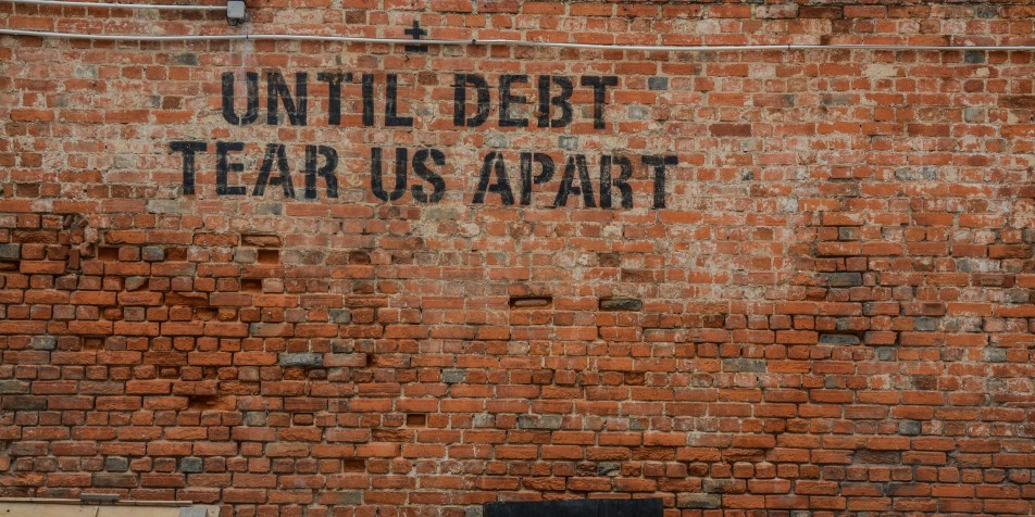 black grafitti on brick wall that reads "Until debt tears us apart."
