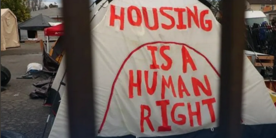 tent with writing in red paint that says "Housing is a human right."