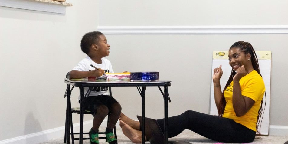A Black mother sitting on the ground talking to a Black child in a chair