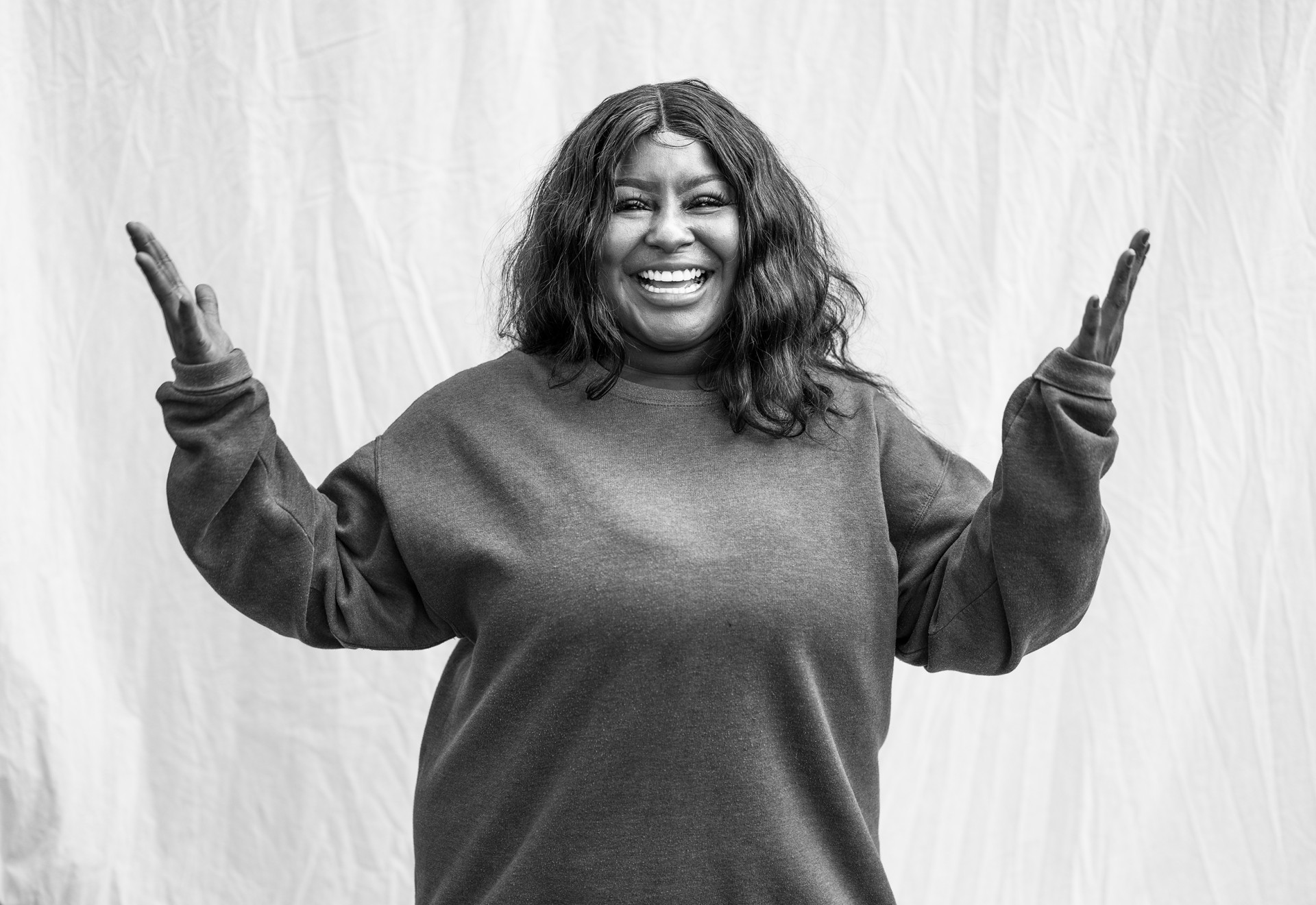 A person in a black sweatshirt smiling with their hands up