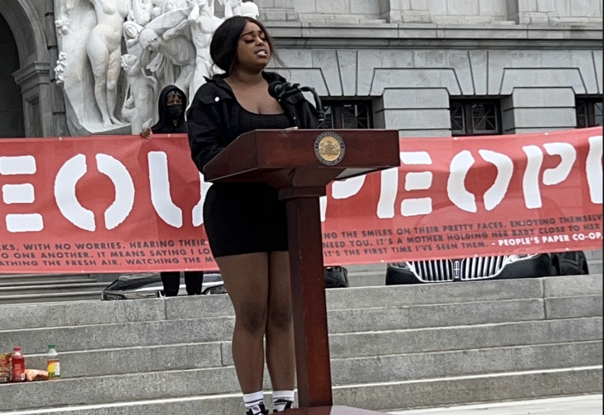 A person speaking at a podium outside a large municipal building.