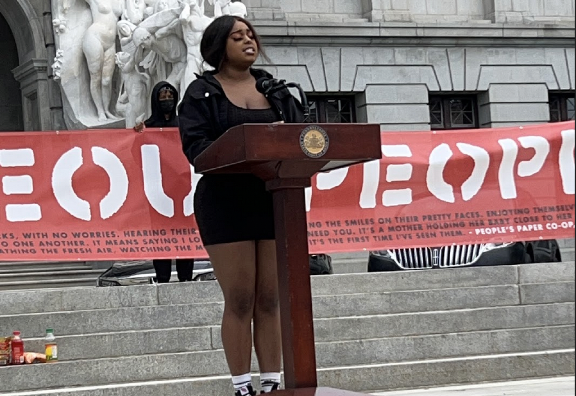 A person speaking at a podium outside a large municipal building. 