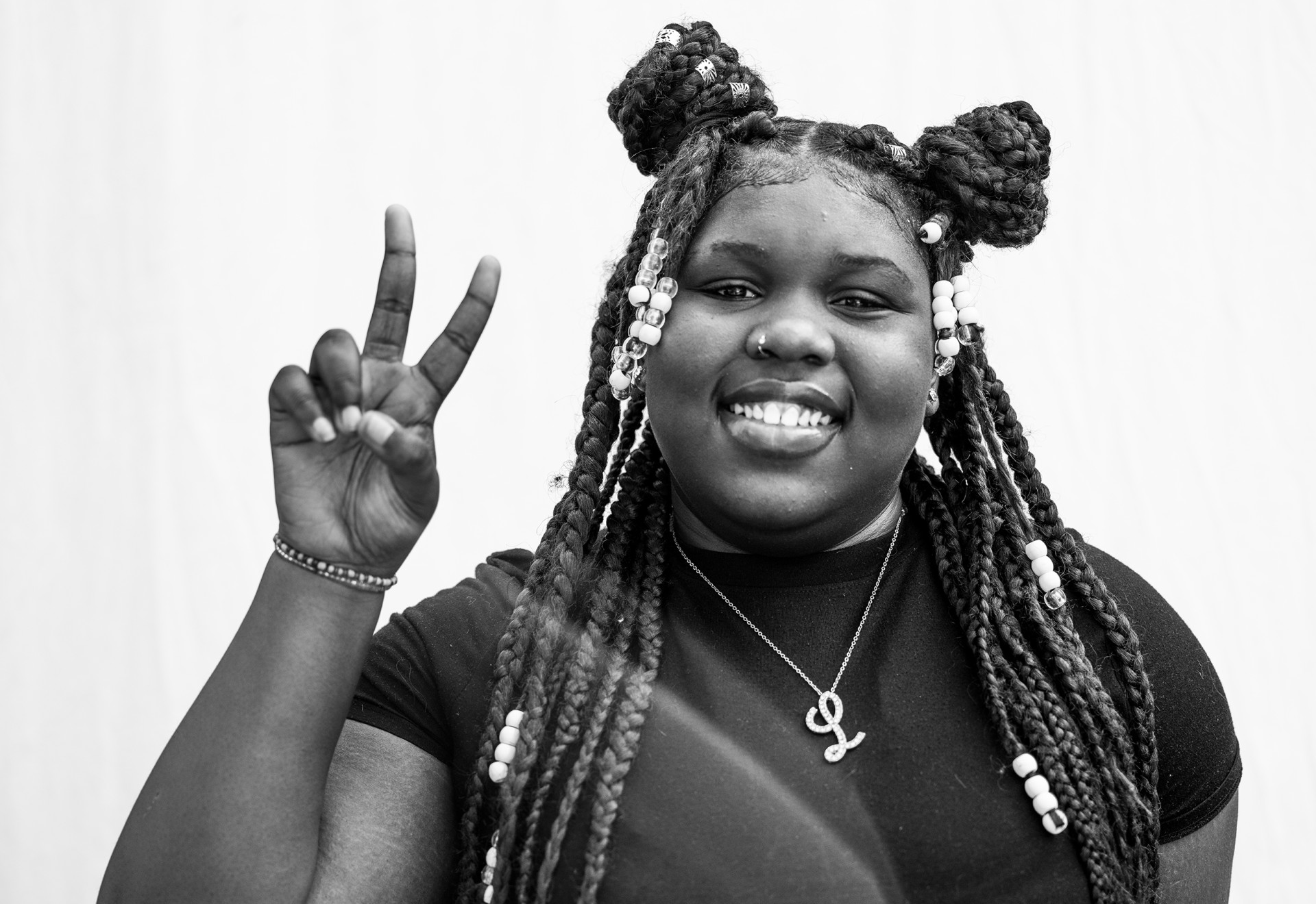 A person with long braids, holding two fingers up as a peace sign and smiling.