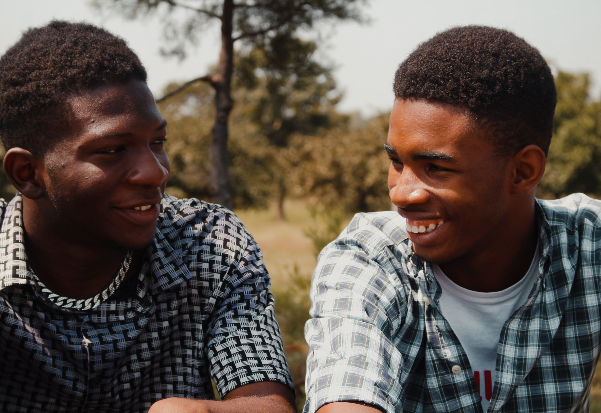 Two boys smiling at each other in the sun.